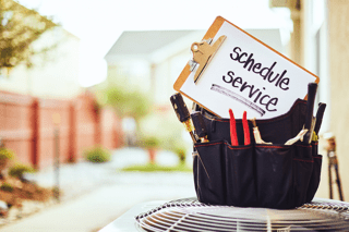 Why Schedule Air Conditioning Maintenance? Toolbox sitting on top of an air conditioning unit with a clip board that reads, 