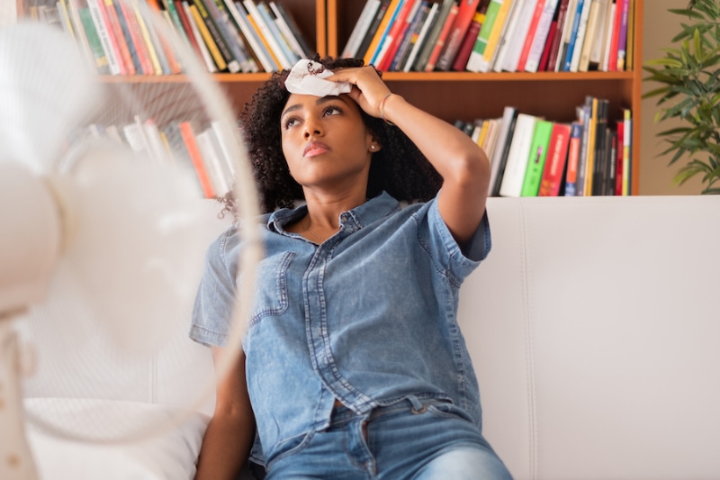 Common AC Problems and Solutions - Black woman sweating and trying to refresh at home.
