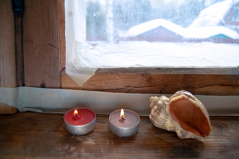 candles lite by a window in winter, How Can I Save Money on My Heating Bill This Winter?