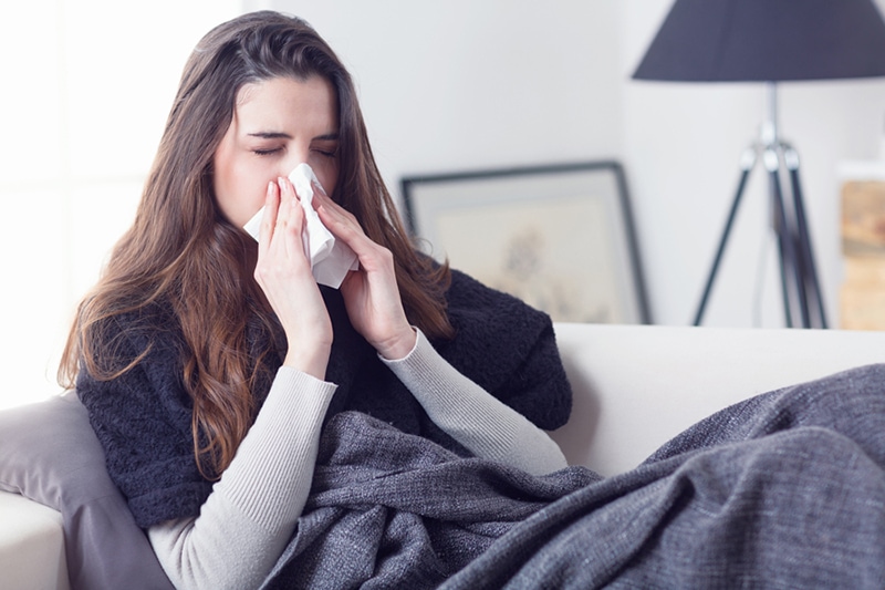 woman blowing her nose on couch